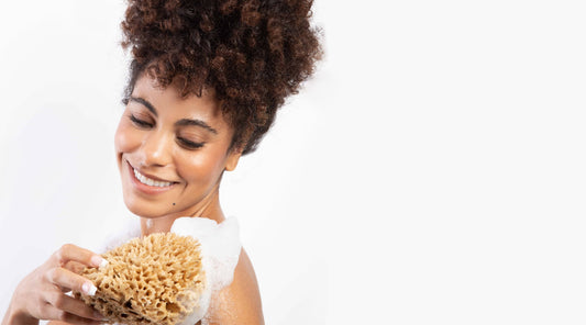 Model holing a soothe sea natural sponge against her shoulder with lather on skin