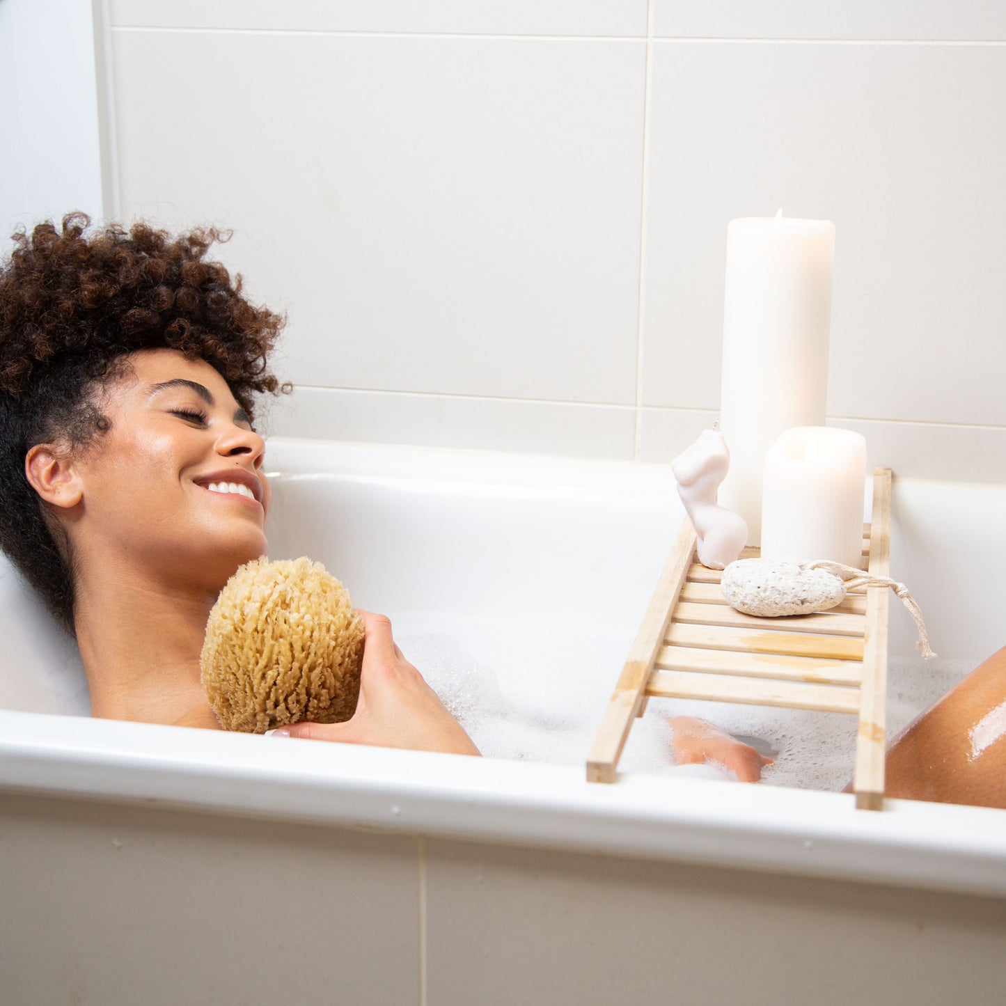 Model in a bath holding a exfoliate natural sea sponge by naroa