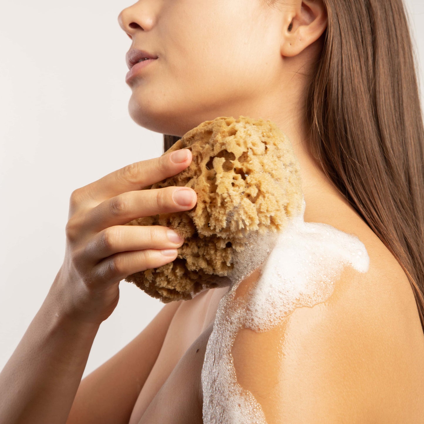 Model holding natural naroa brown massage sponge against her shoulder with lather foam