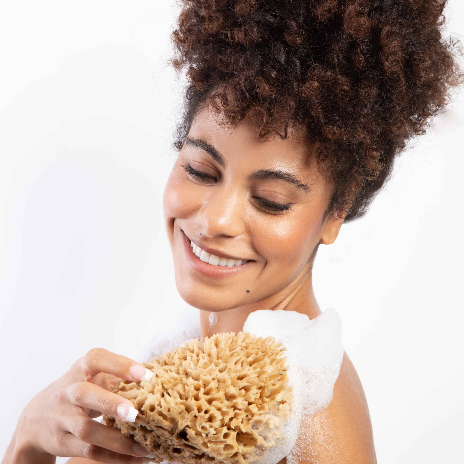 Smiling model holding a Naroa soothe sponge using it on her shoulder with lather foam